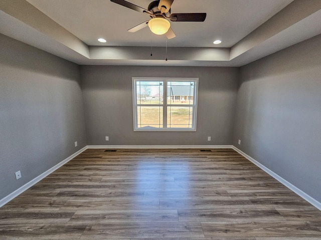 empty room with ceiling fan, a raised ceiling, and hardwood / wood-style floors