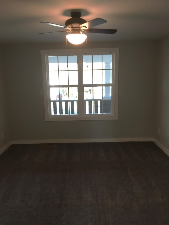 spare room featuring dark colored carpet and ceiling fan