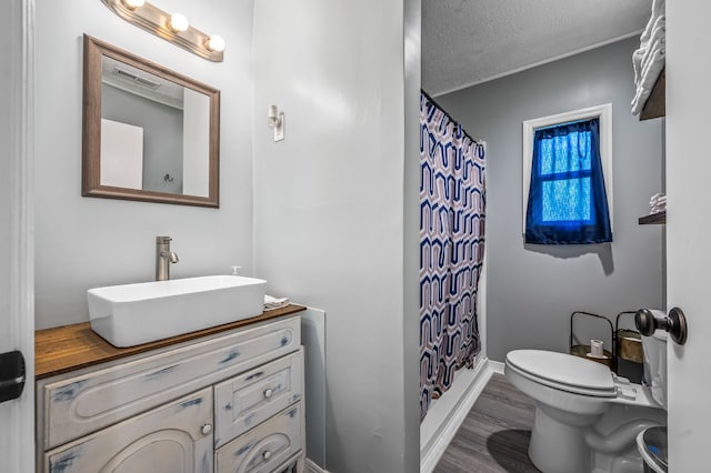 bathroom with walk in shower, wood-type flooring, a textured ceiling, toilet, and vanity