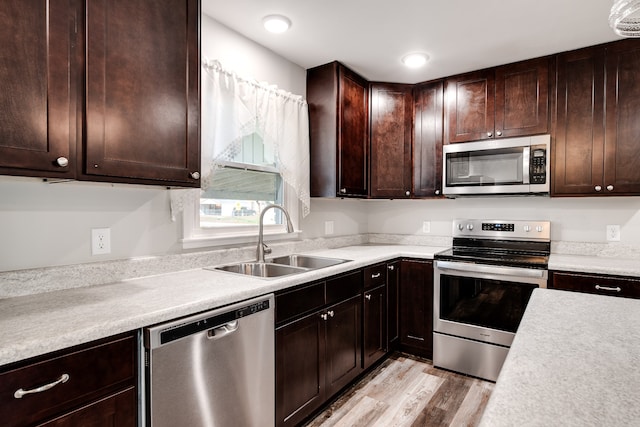 kitchen with dark brown cabinetry, sink, stainless steel appliances, and light hardwood / wood-style flooring