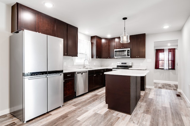 kitchen with light wood-type flooring, stainless steel appliances, sink, a kitchen island, and hanging light fixtures