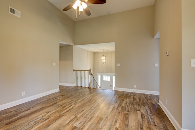 spare room with ceiling fan with notable chandelier, wood-type flooring, and a towering ceiling