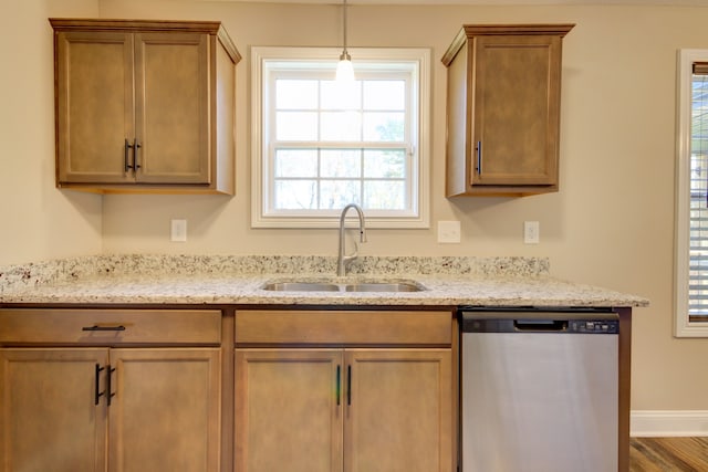 kitchen with pendant lighting, hardwood / wood-style floors, sink, stainless steel dishwasher, and light stone countertops