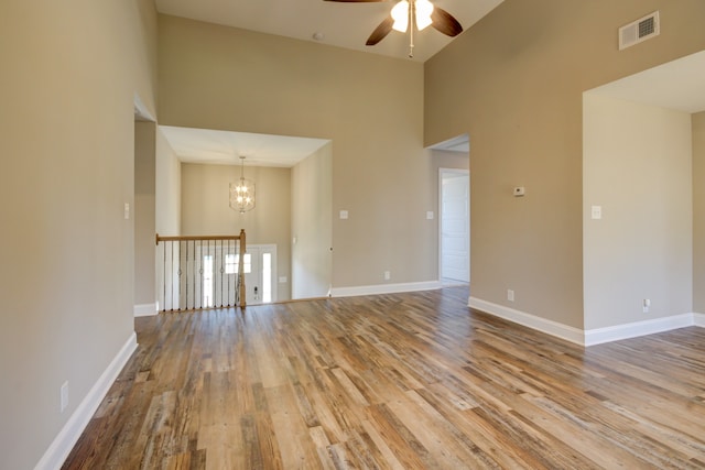 unfurnished room with ceiling fan with notable chandelier, light hardwood / wood-style floors, and a towering ceiling