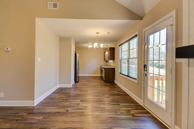 interior space featuring dark wood-type flooring, vaulted ceiling, stainless steel fridge, decorative light fixtures, and a chandelier