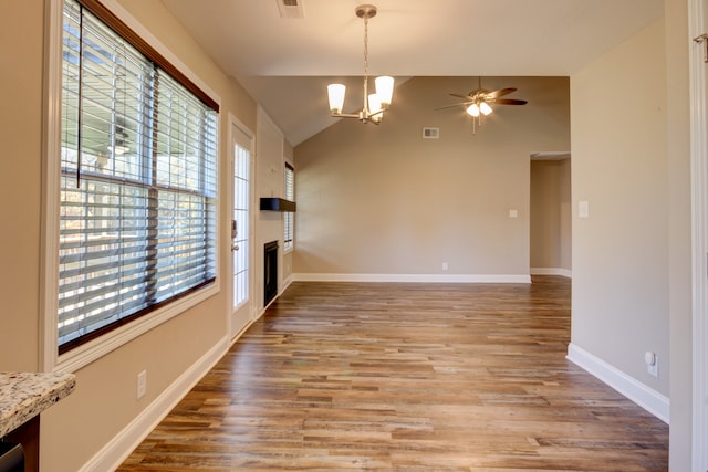 unfurnished living room with vaulted ceiling, plenty of natural light, wood-type flooring, and ceiling fan with notable chandelier