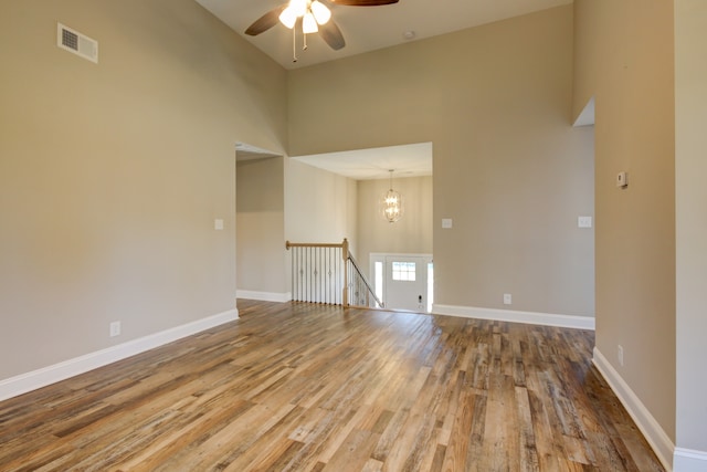 empty room with ceiling fan with notable chandelier, a towering ceiling, and hardwood / wood-style flooring