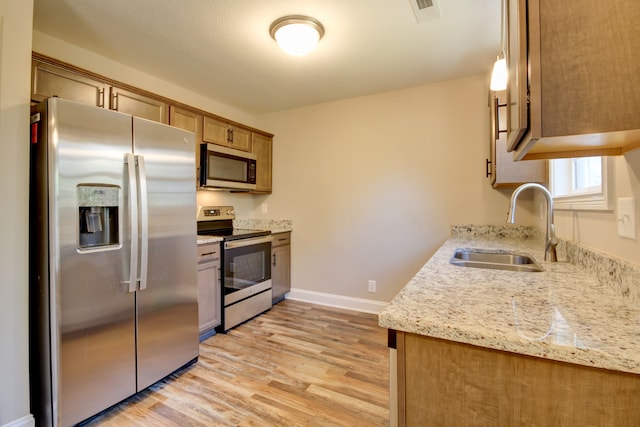 kitchen featuring sink, stainless steel appliances, light stone counters, light hardwood / wood-style flooring, and decorative light fixtures