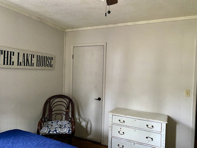 bedroom with ceiling fan, wood walls, dark wood-type flooring, and a textured ceiling