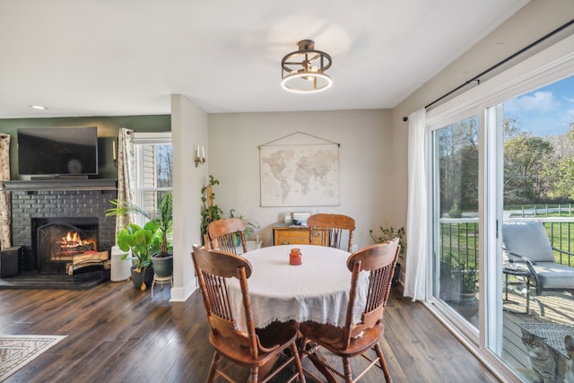 dining room with an inviting chandelier, a brick fireplace, and dark wood-type flooring