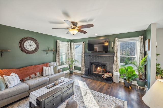 living room featuring ceiling fan, dark wood-type flooring, a healthy amount of sunlight, and a brick fireplace