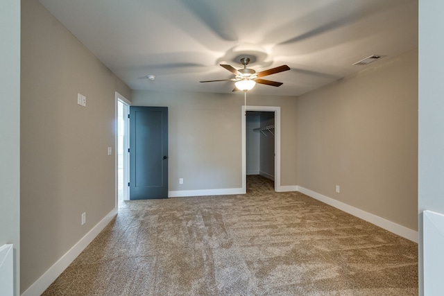 unfurnished bedroom featuring a spacious closet, a closet, ceiling fan, and light colored carpet