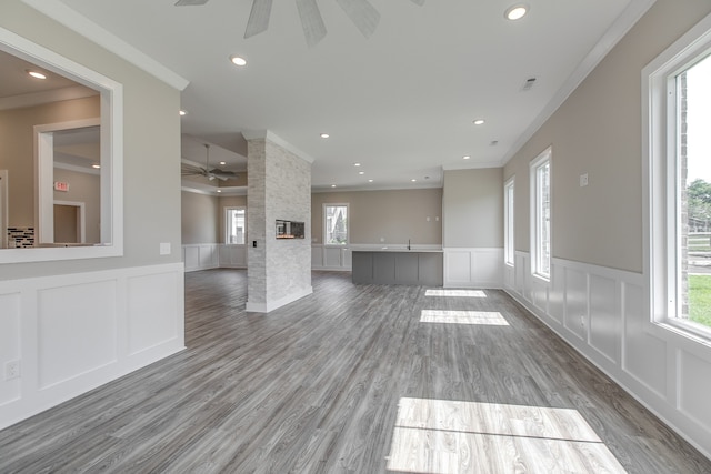 unfurnished living room with a fireplace, wood-type flooring, ceiling fan, and ornamental molding