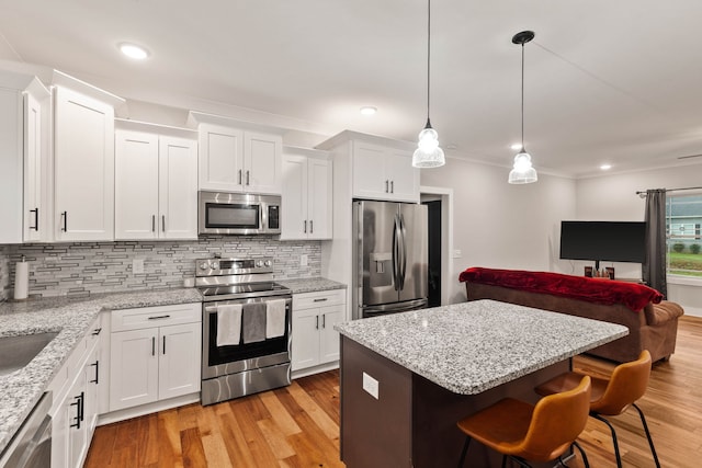 kitchen featuring stainless steel appliances, decorative light fixtures, light hardwood / wood-style flooring, white cabinets, and a kitchen island