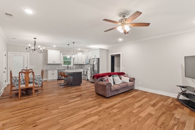 living room with ceiling fan with notable chandelier, light hardwood / wood-style flooring, crown molding, and sink