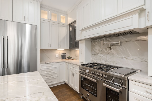 kitchen with light stone countertops, backsplash, appliances with stainless steel finishes, white cabinets, and custom exhaust hood