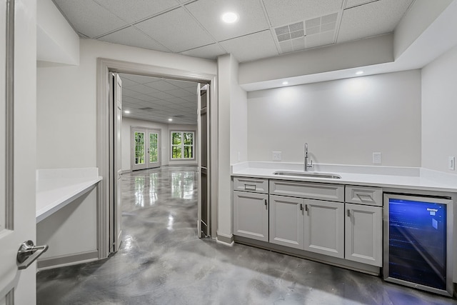 bar featuring a paneled ceiling, beverage cooler, sink, concrete floors, and gray cabinets