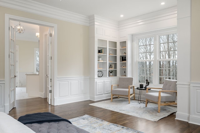 sitting room featuring built in shelves, dark hardwood / wood-style flooring, a notable chandelier, and ornamental molding