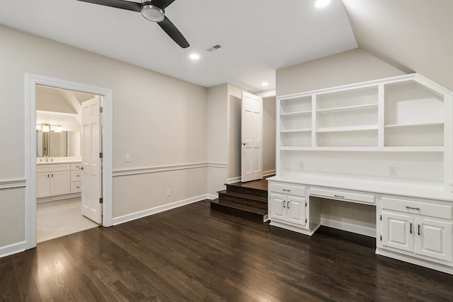 unfurnished office with vaulted ceiling, ceiling fan, built in desk, and dark hardwood / wood-style floors