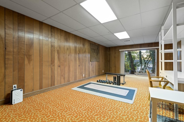 interior space featuring carpet flooring, a drop ceiling, and wood walls