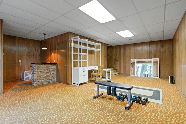 exercise area with carpet flooring, wooden walls, and a drop ceiling