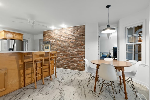 dining space featuring a wood stove, ceiling fan, and brick wall