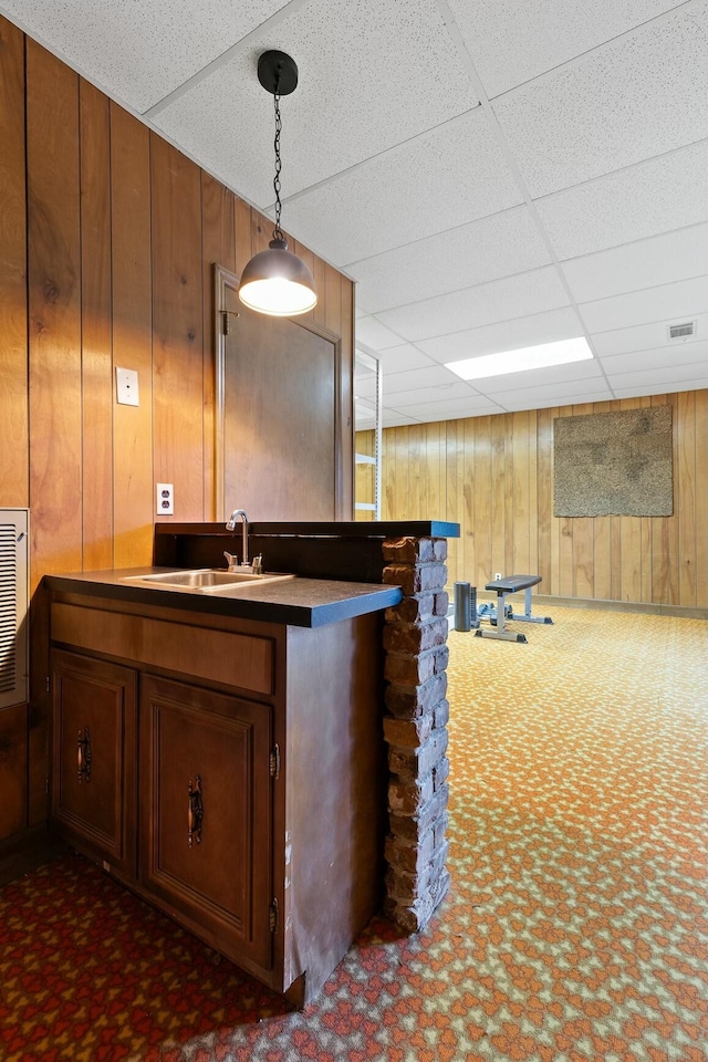 bar with a paneled ceiling, wood walls, dark colored carpet, sink, and decorative light fixtures