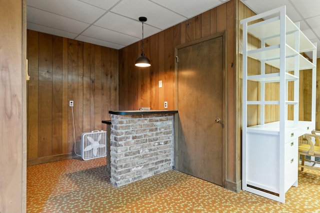 bar featuring wooden walls, a drop ceiling, and decorative light fixtures