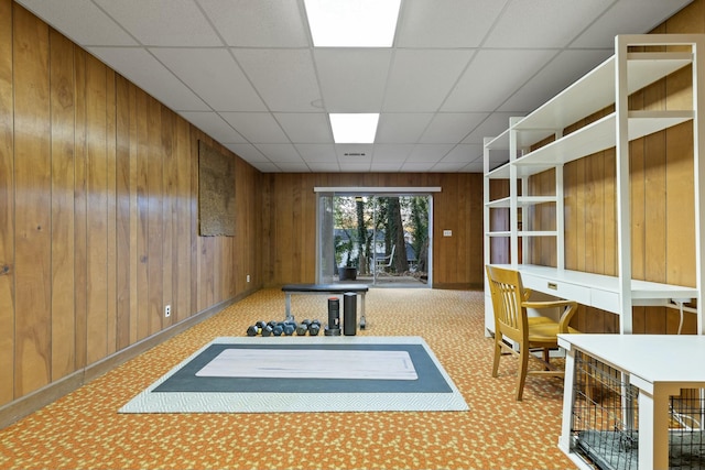 interior space featuring a paneled ceiling, light colored carpet, and wood walls