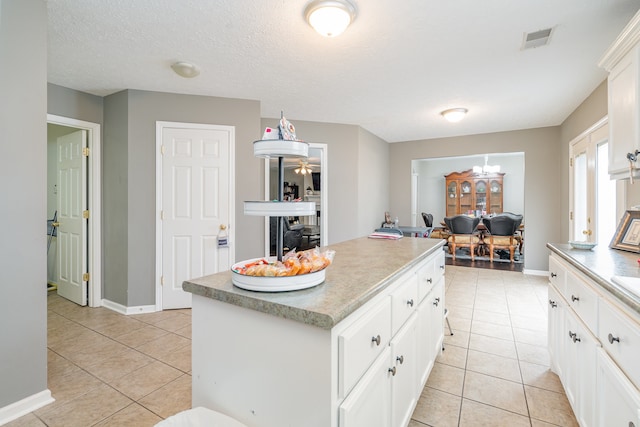 kitchen featuring a textured ceiling, white cabinets, a kitchen island, and light tile patterned floors