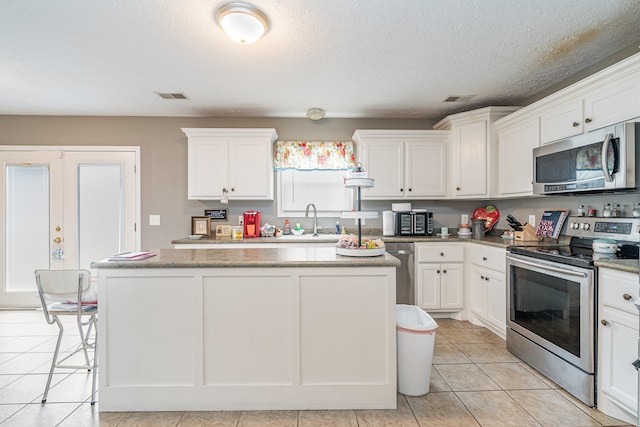 kitchen with white cabinets, a center island, stainless steel appliances, and a textured ceiling