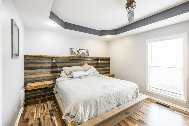 bedroom with wood-type flooring and a raised ceiling