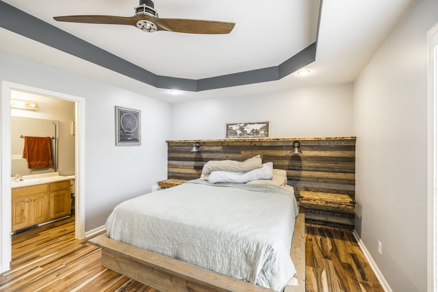 bedroom with a tray ceiling, ceiling fan, sink, hardwood / wood-style floors, and connected bathroom