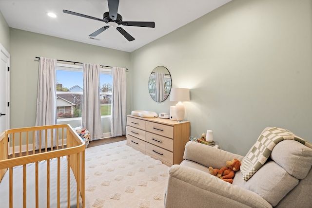 bedroom with ceiling fan, a nursery area, and light wood-type flooring