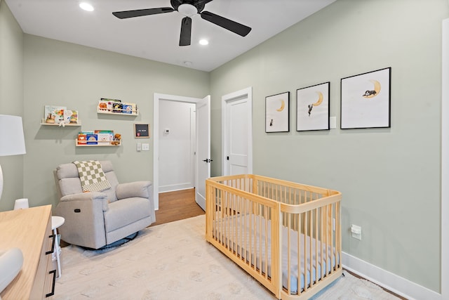 bedroom with light wood-type flooring, a nursery area, and ceiling fan