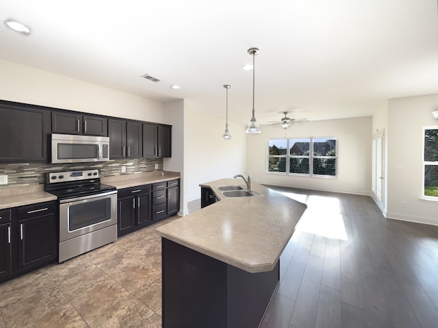 kitchen featuring appliances with stainless steel finishes, backsplash, a kitchen island with sink, sink, and hanging light fixtures