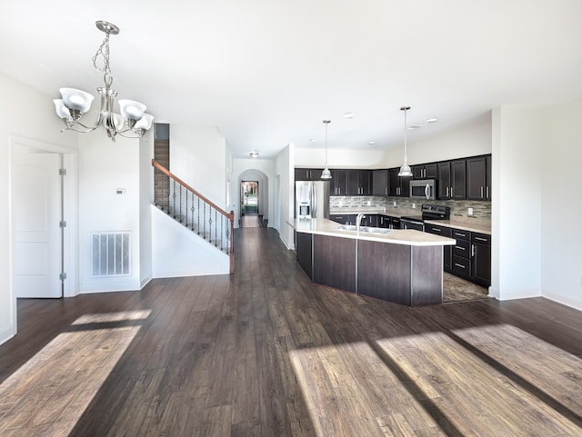 kitchen featuring appliances with stainless steel finishes, dark wood-type flooring, sink, a center island with sink, and a notable chandelier