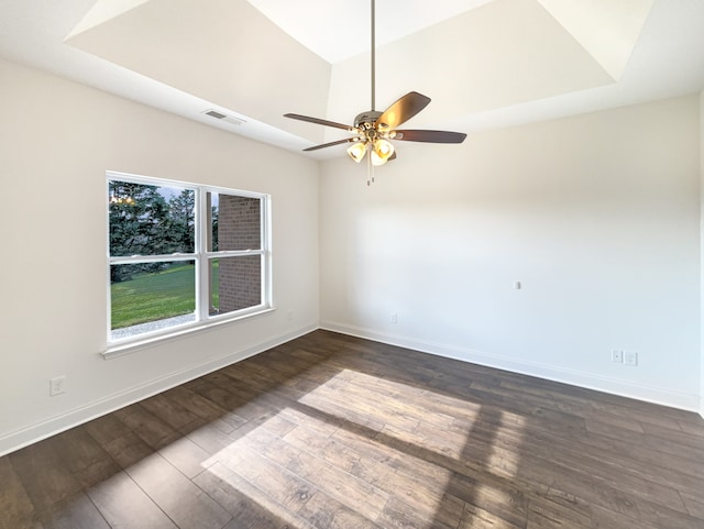 empty room featuring dark hardwood / wood-style floors, ceiling fan, and a tray ceiling