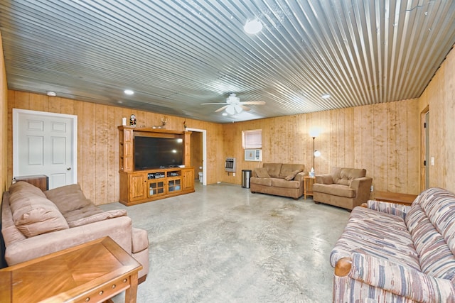 living room featuring ceiling fan, wood walls, concrete flooring, and heating unit