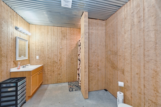 bathroom featuring wooden walls, vanity, and concrete flooring