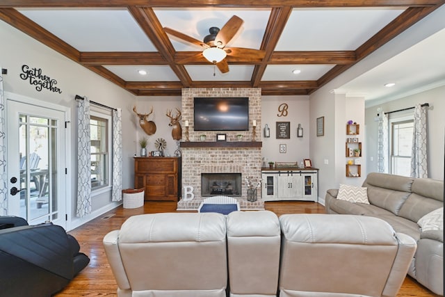 living room with ceiling fan, coffered ceiling, light hardwood / wood-style flooring, beamed ceiling, and a fireplace