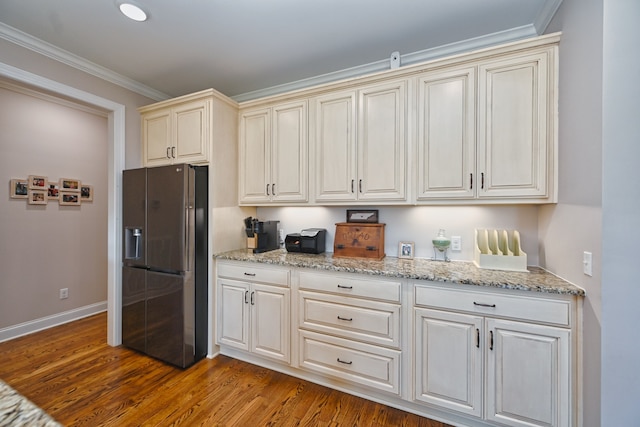 kitchen featuring light stone countertops, stainless steel refrigerator with ice dispenser, ornamental molding, cream cabinets, and wood-type flooring