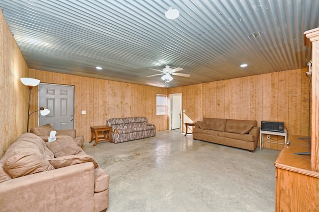 living room with concrete floors, ceiling fan, and wood walls