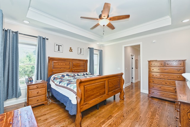 bedroom featuring light wood-type flooring, a tray ceiling, ceiling fan, and crown molding