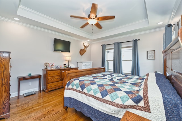 bedroom with light wood-type flooring, a raised ceiling, ceiling fan, and crown molding