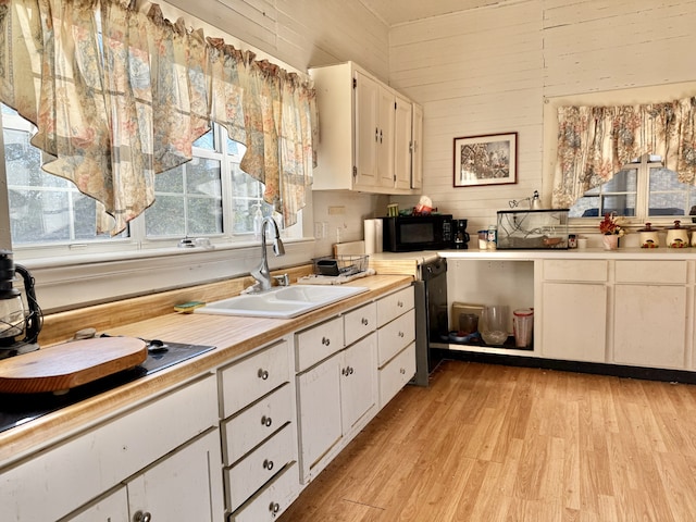 kitchen featuring dishwasher, white cabinets, sink, wooden walls, and light hardwood / wood-style flooring