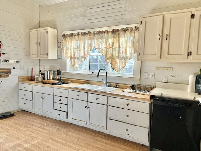 kitchen with wood walls, dishwasher, light wood-type flooring, and sink