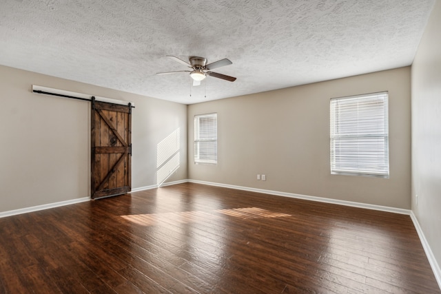 unfurnished room with a textured ceiling, ceiling fan, a barn door, and dark wood-type flooring