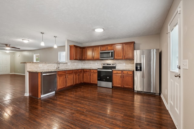 kitchen featuring kitchen peninsula, stainless steel appliances, ceiling fan, dark wood-type flooring, and hanging light fixtures