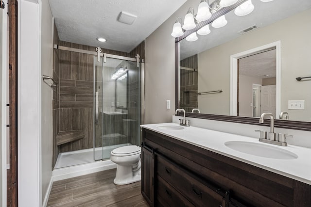 bathroom featuring vanity, a textured ceiling, hardwood / wood-style floors, toilet, and a shower with shower door